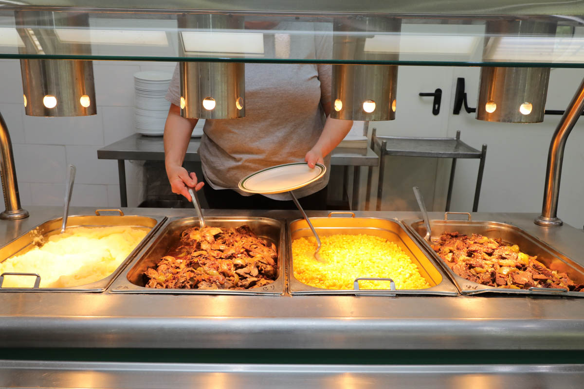 עובדת של חדר האוכל מגישה אוכל מהפס החם